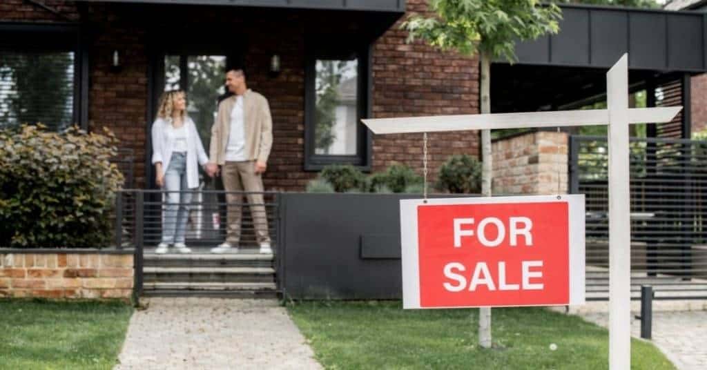 Couple standing in front of a modern brick house with a 'For Sale' sign in the garden. – Ghar.ie property listing
