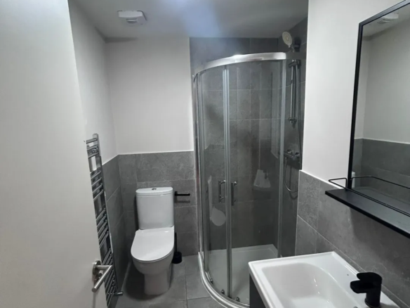 Modern gray bathroom with shower, toilet, sink, and towel rack.