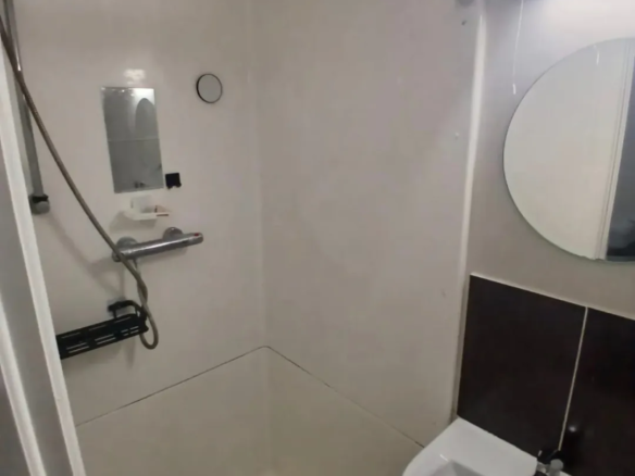 Small bathroom shower with sink, mirror, and white walls.