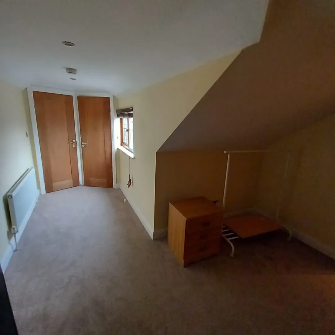 Attic Bedroom Sloped Ceiling Furniture Attic bedroom with sloped ceiling, wardrobe, dresser, and clothes rack.