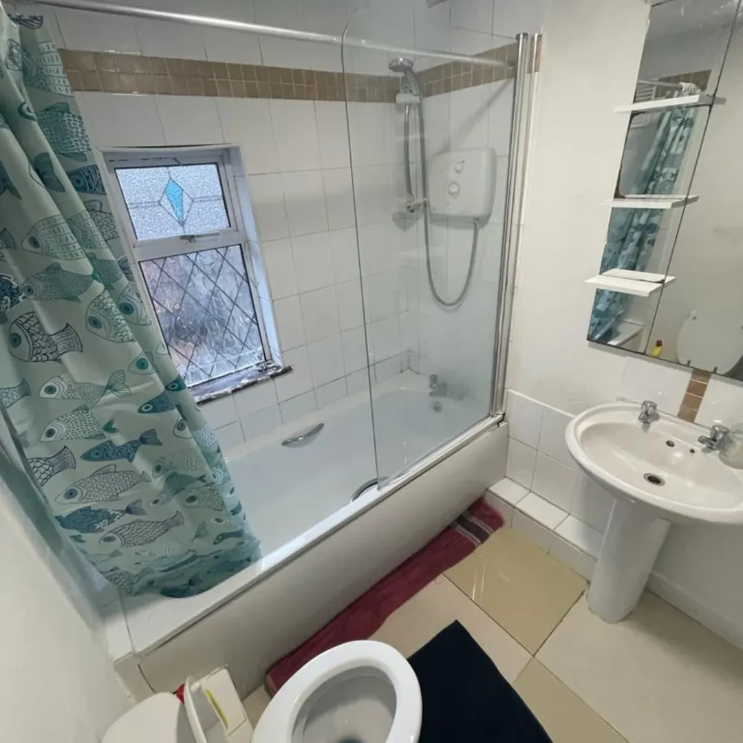 Bathroom with tub, shower, toilet, sink, and fish-themed shower curtain.