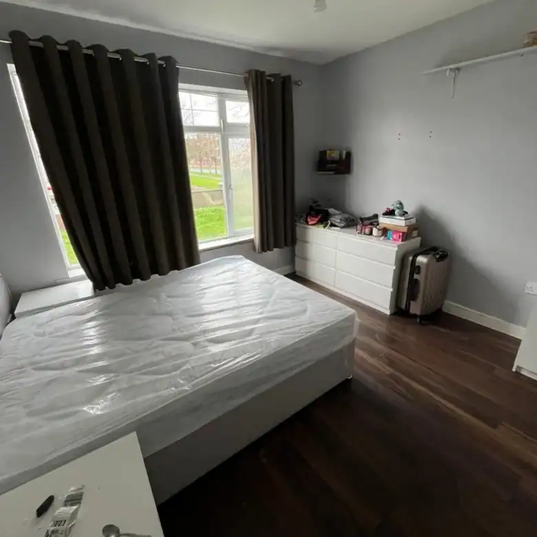 Bedroom with a bed, dresser, suitcase, and dark curtains in front of a window.