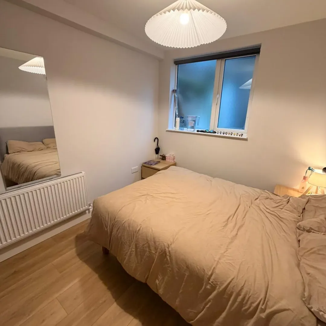 Cozy bedroom with bed, bedside table, radiator, mirror, and window.