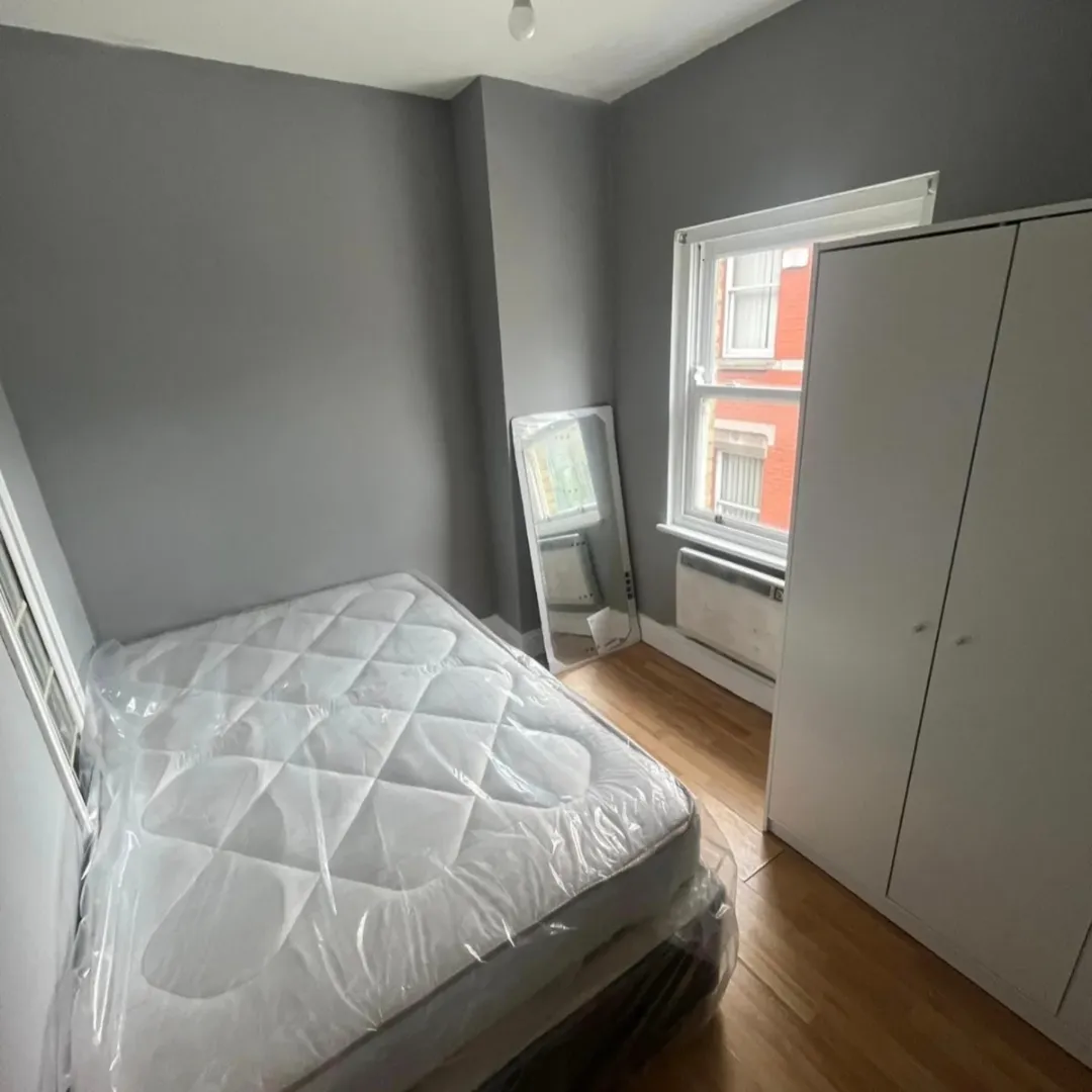 Bedroom with bed, wardrobe, mirror, and window. Gray walls and wood floor.