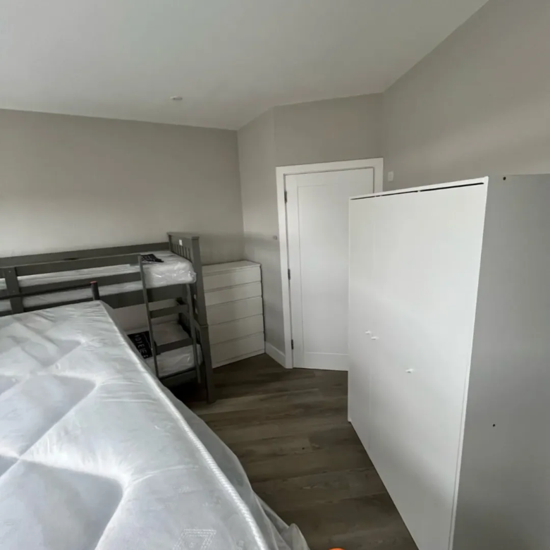 Bedroom with bunk bed, dresser, and white wardrobe. Neutral decor.