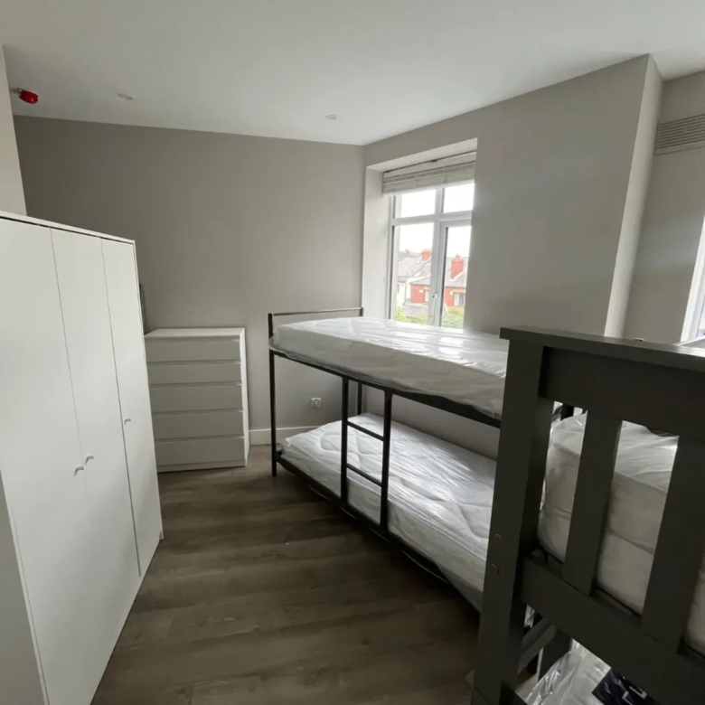 Bedroom with bunk bed, white wardrobe, and chest of drawers. Neutral tones.