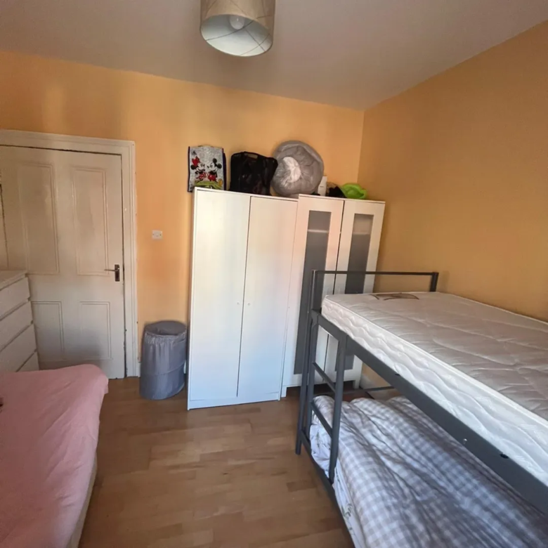 Bedroom with bunk beds, wardrobe, and pink single bed against yellow walls.
