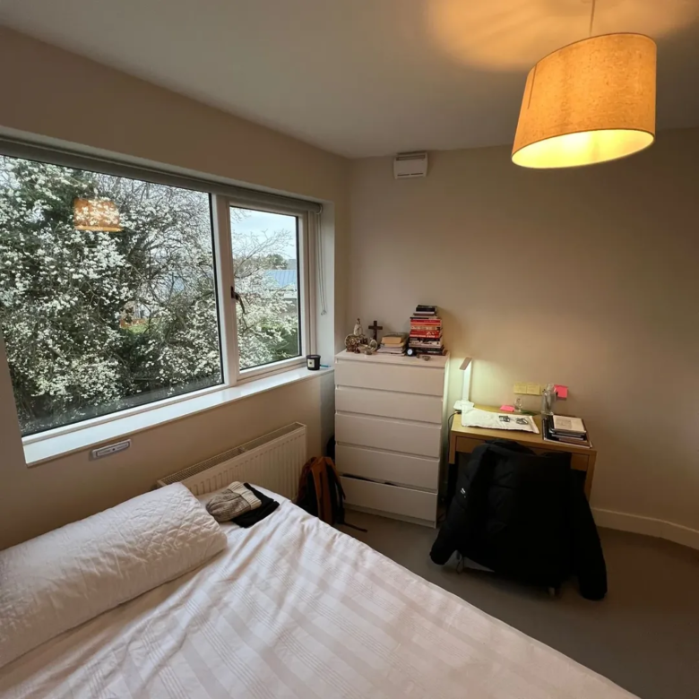 Bedroom interior with bed, desk, dresser, and window view of blossoming trees.