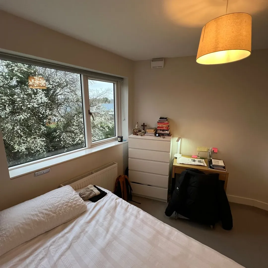 Bedroom interior with bed, desk, dresser, and window view of blossoming trees.