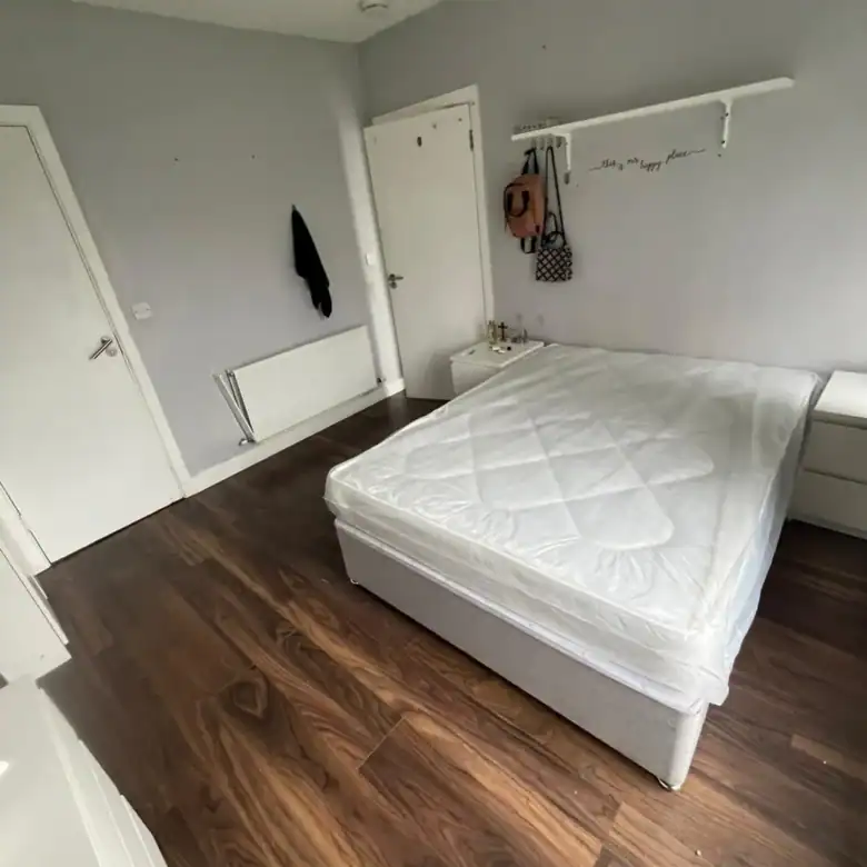 Bedroom with new mattress on bed, wood floor, and white walls.