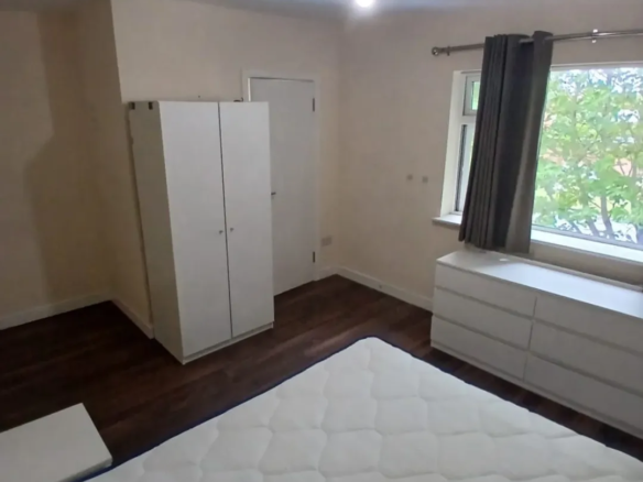 Bedroom with white bed, wardrobe, dresser, and gray curtained window.