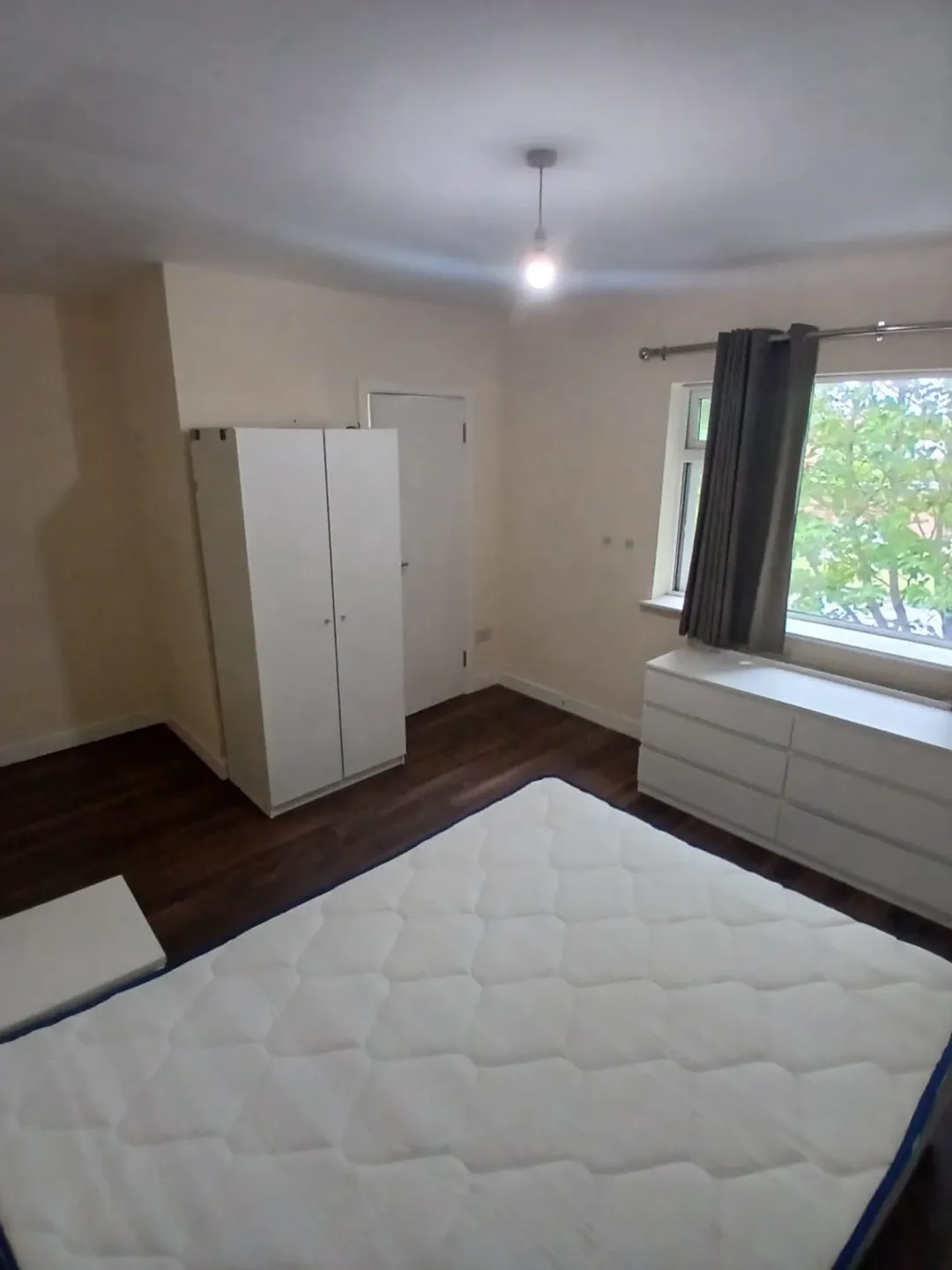Bedroom with white bed, wardrobe, dresser, and gray curtained window.