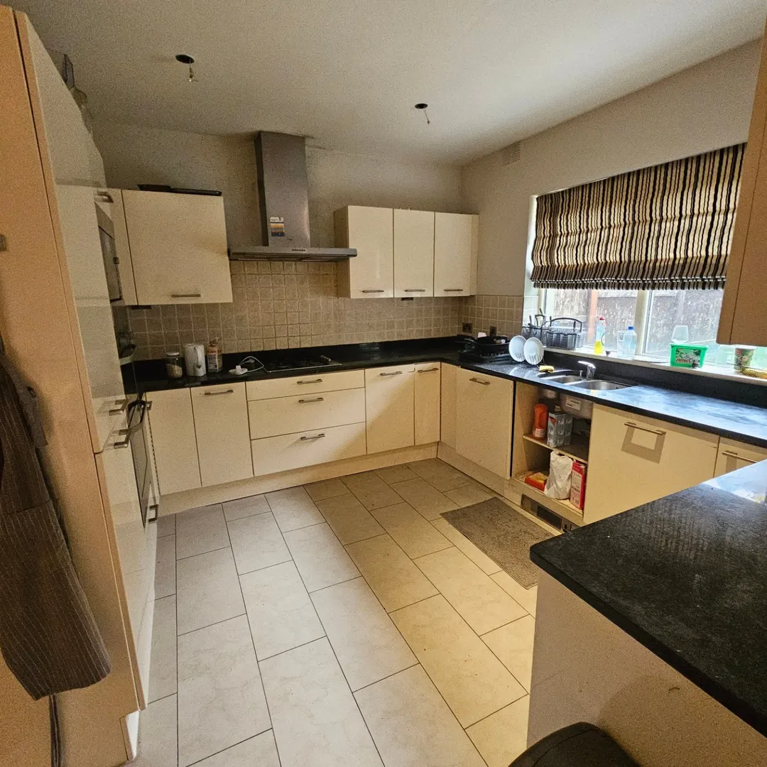 Beige kitchen with cream cabinets, black countertops, and tile flooring.