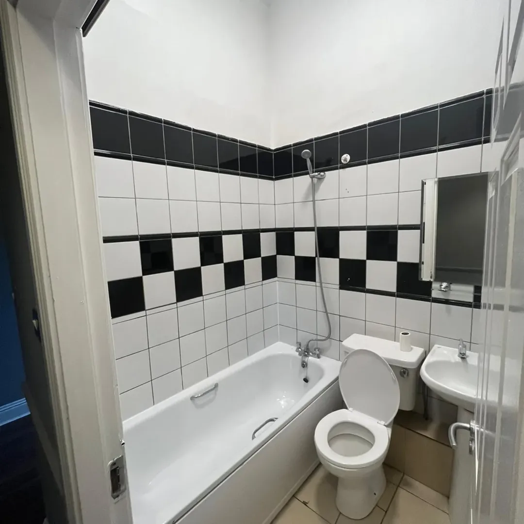Bathroom with white suite, black and white checkered tile, and shower.