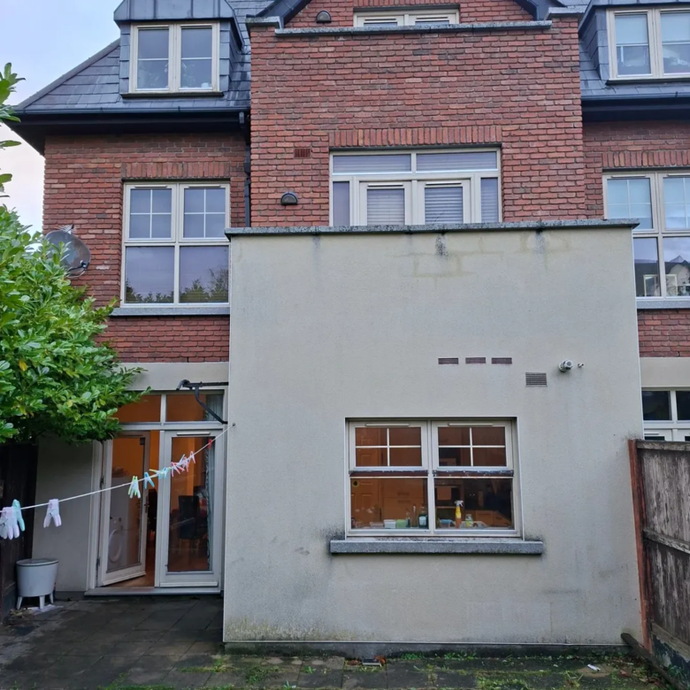 Exterior view of a two-story brick house with a gray extension and clothesline in the backyard.
