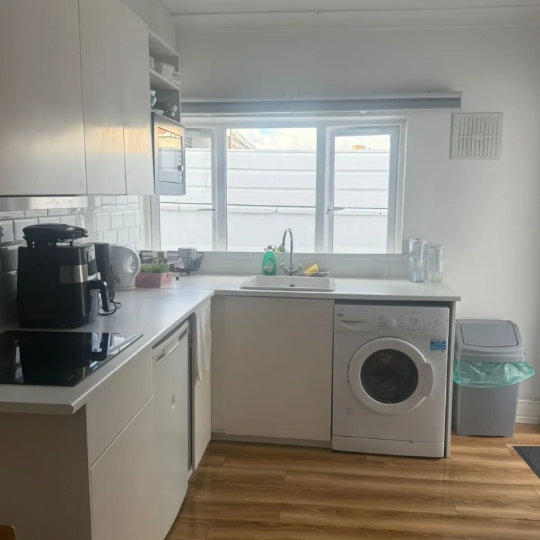 Bright kitchen with white cabinets, washing machine, and window above sink.
