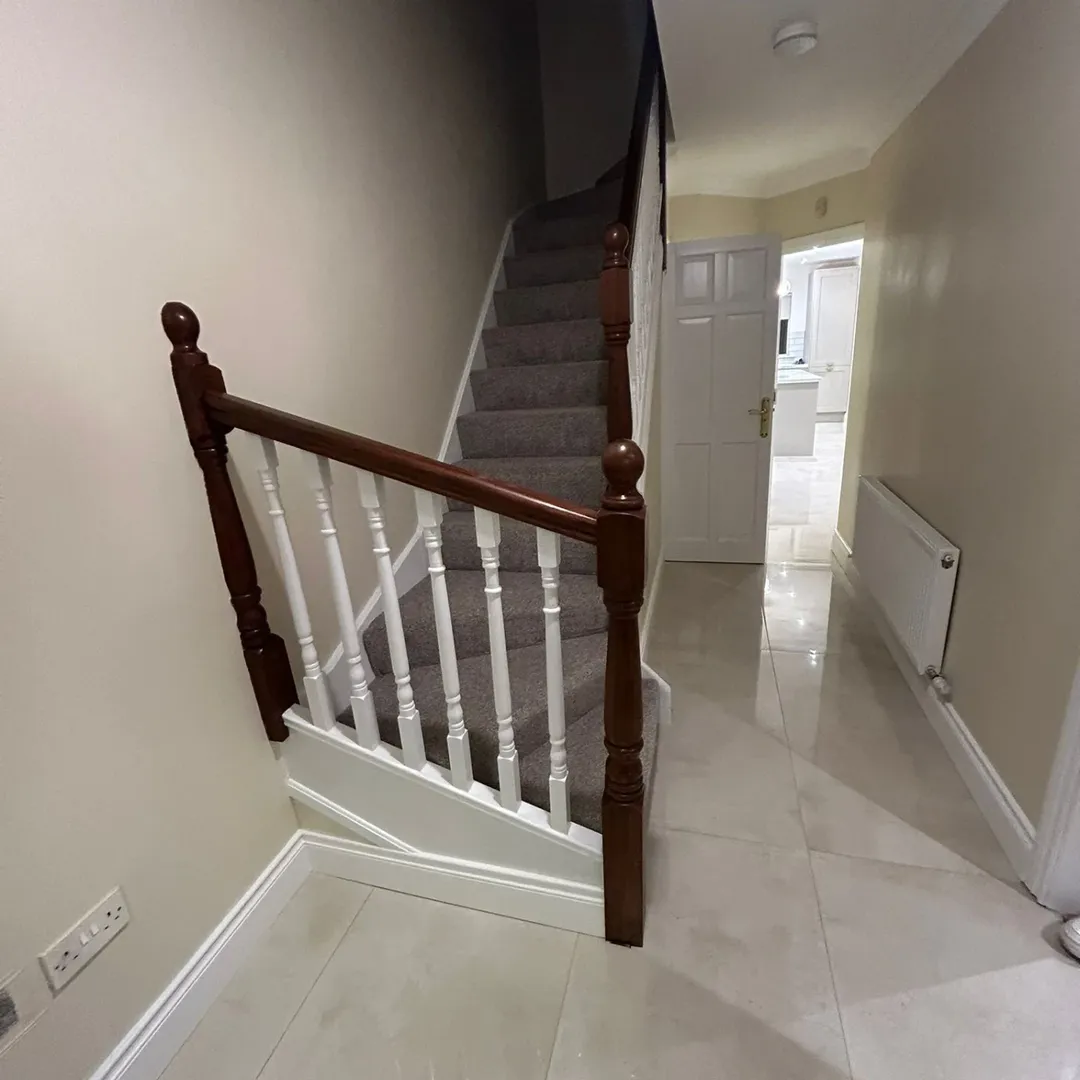 Carpeted Stairs White Spindles Wood Banister Hallway with carpeted stairs, white spindles, and dark wood banister leading to an open doorway.