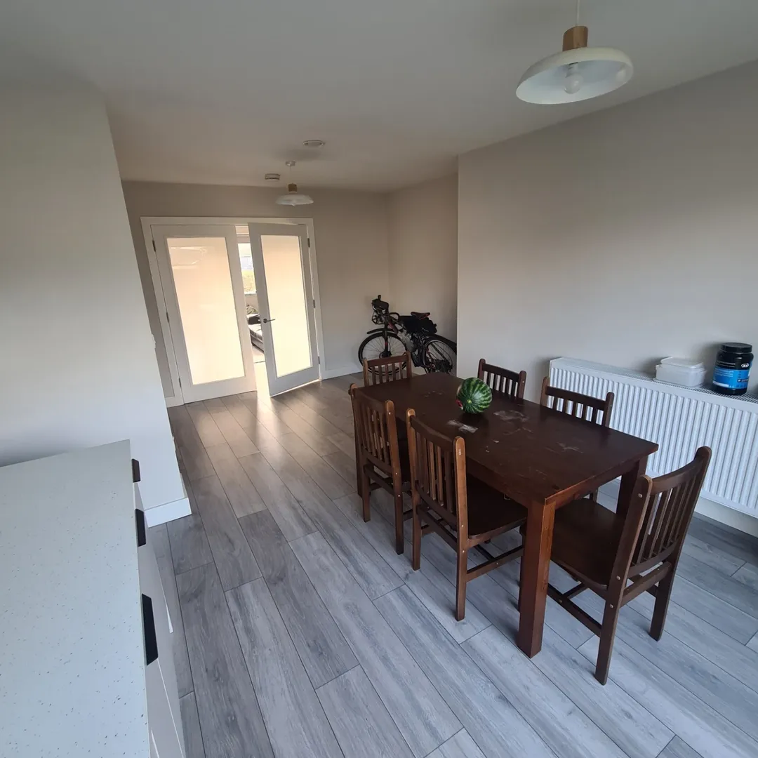 Dining room with wooden table, chairs, and gray flooring, natural light.