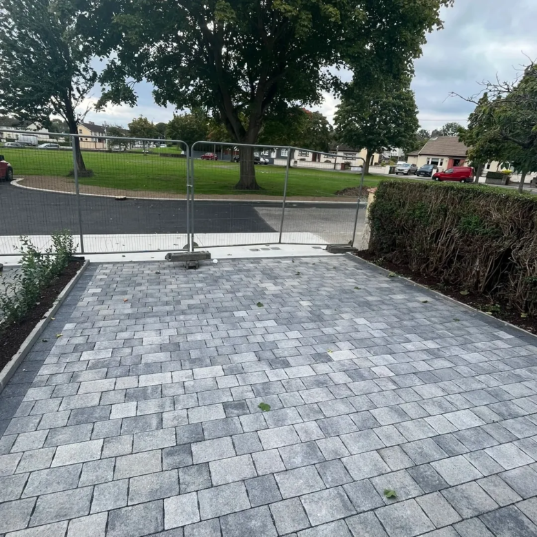 Newly paved gray brick driveway with fresh landscaping and temporary fencing.