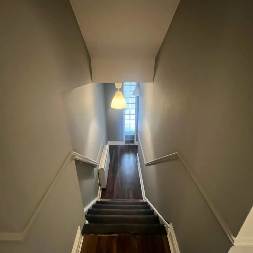 Stairway view from top with gray walls, dark carpet stairs, and glass block window at the bottom.