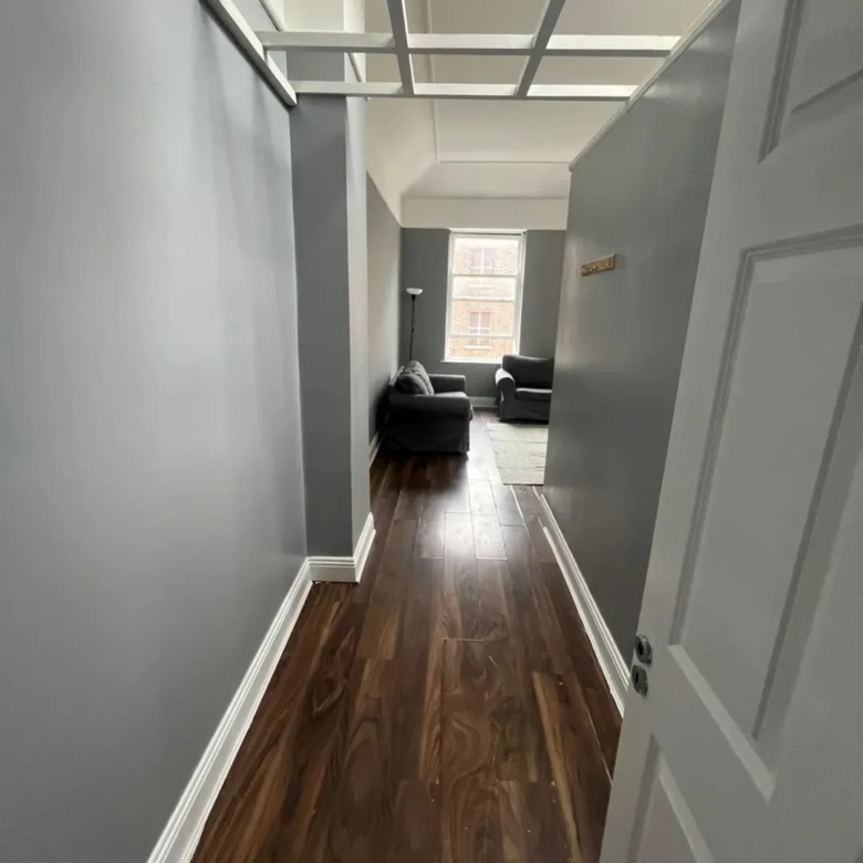 Hallway view with gray walls, dark wood floors, and seating area beyond.