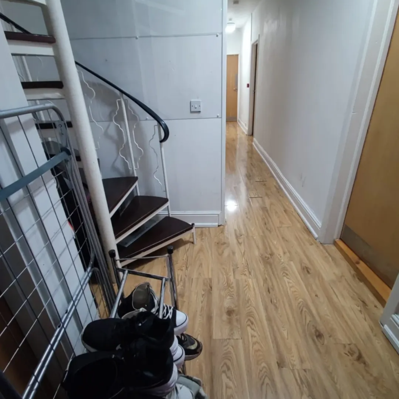 Hallway with spiral staircase, shoes, and drying rack.