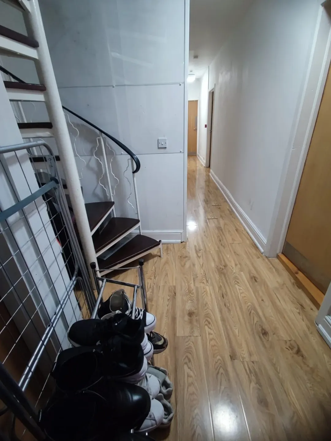 Hallway with spiral staircase, shoes, and drying rack.