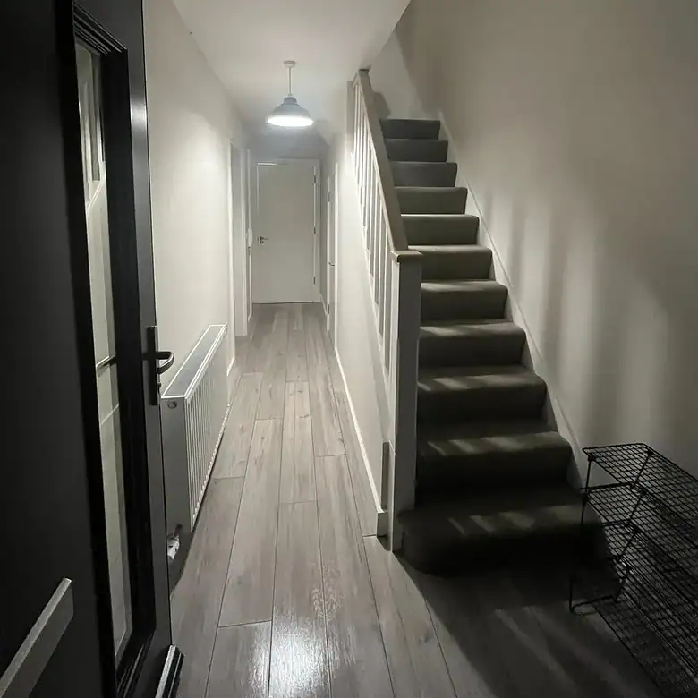 Hallway with stairs and gray wood-look flooring, white walls, and black door.