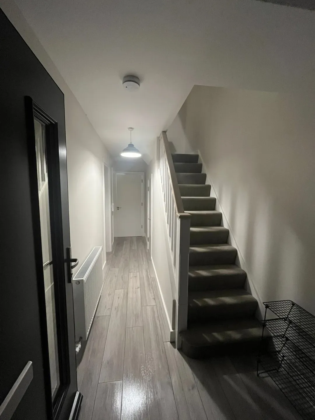 Hallway with stairs and gray wood-look flooring, white walls, and black door.