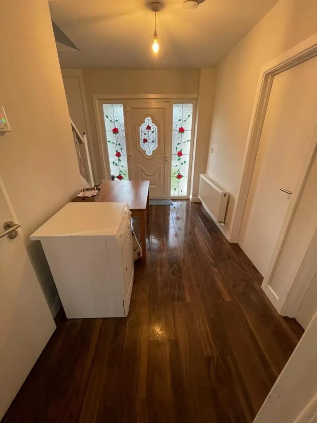 Hallway with dark wood floors, white walls, rose-decorated door, and white cabinet.