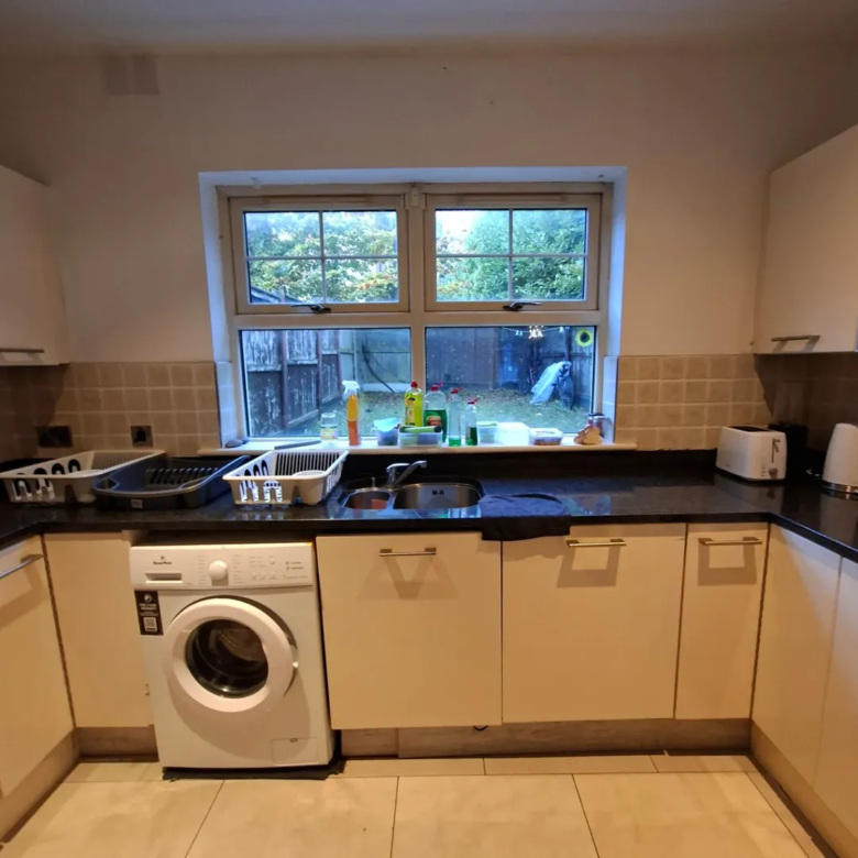 Kitchen interior with washing machine, sink, and window overlooking garden.