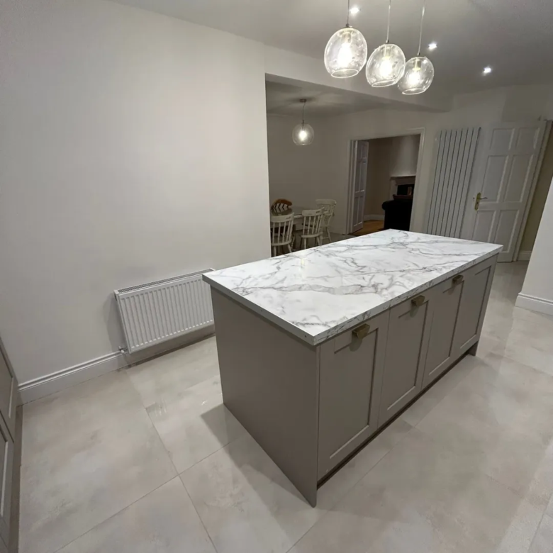 Kitchen island with marble countertop and gray cabinets under pendant lights.