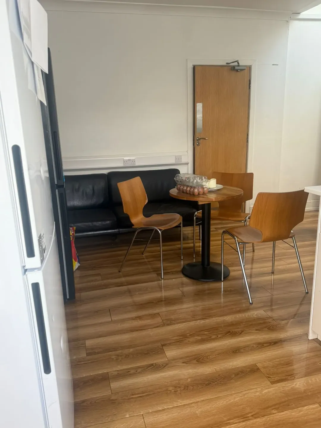 Modern kitchen area with table, chairs, and black sofa. Bright and clean.