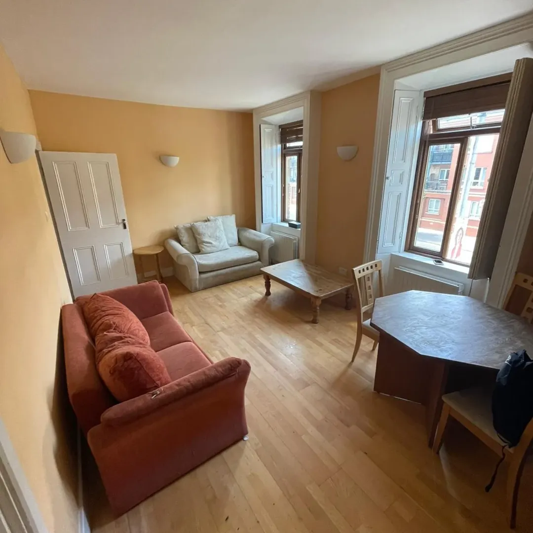Cozy living room with sofa, loveseat, dining table, and windows. Natural light and warm color scheme.