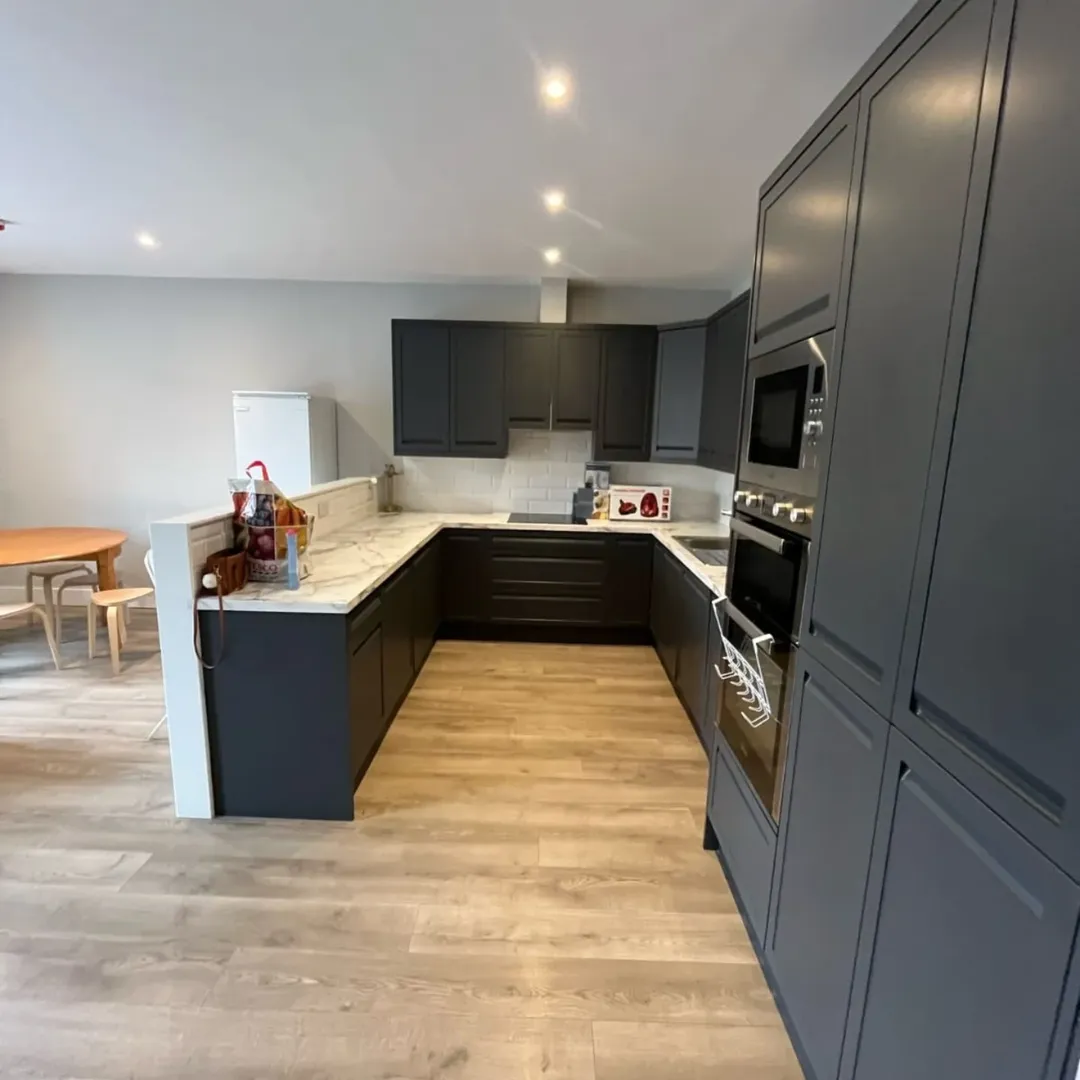 Modern kitchen with dark gray cabinets, marble countertops, and light wood flooring.