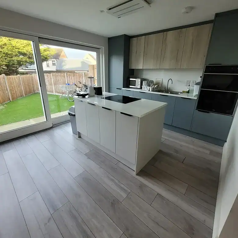 Modern kitchen with island, grey cabinets, wood accents, and garden view.