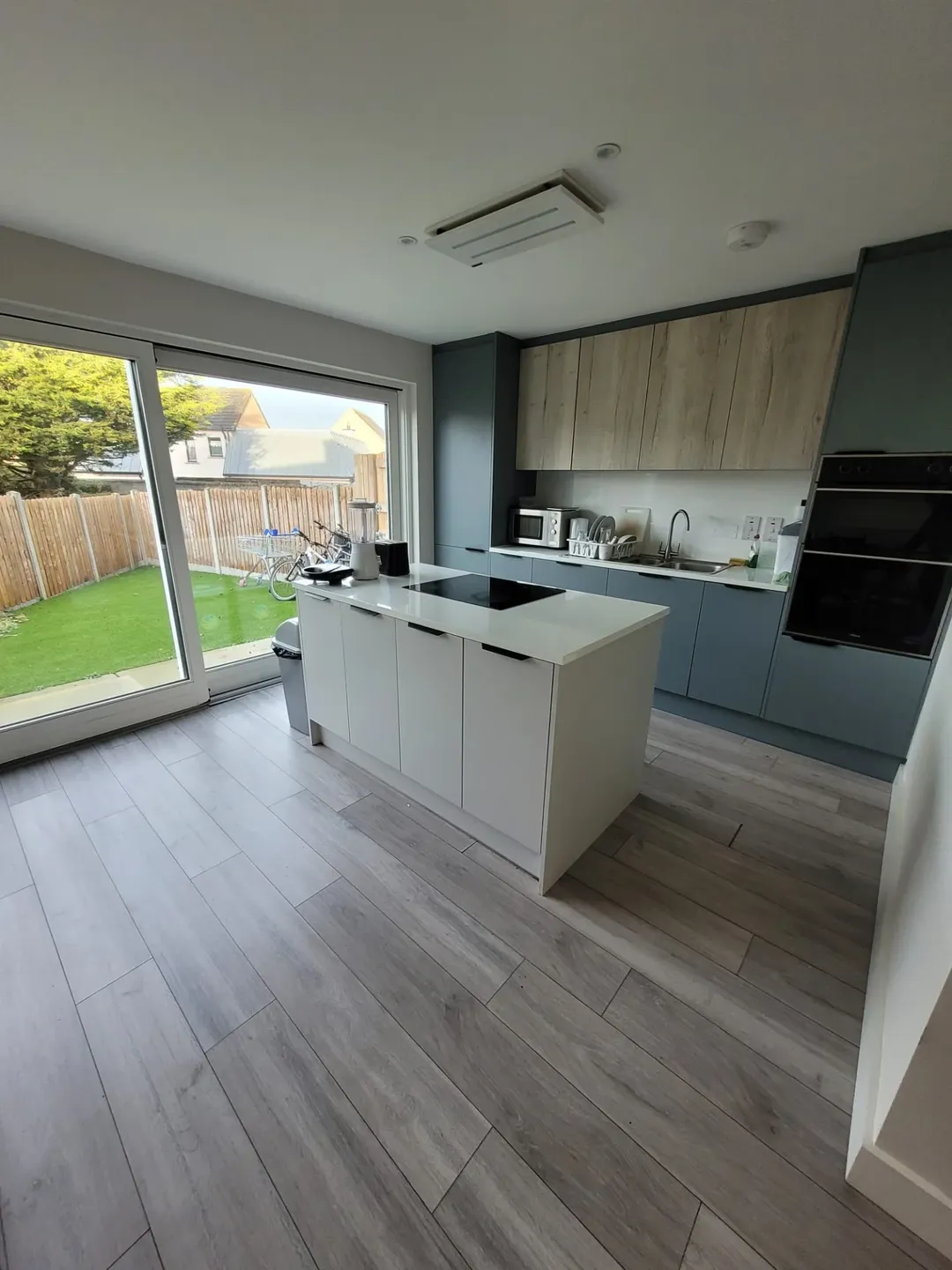 Modern kitchen with island, grey cabinets, wood accents, and garden view.
