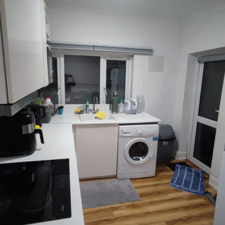 Modern kitchen with white cabinets, washing machine, and wood-look flooring.
