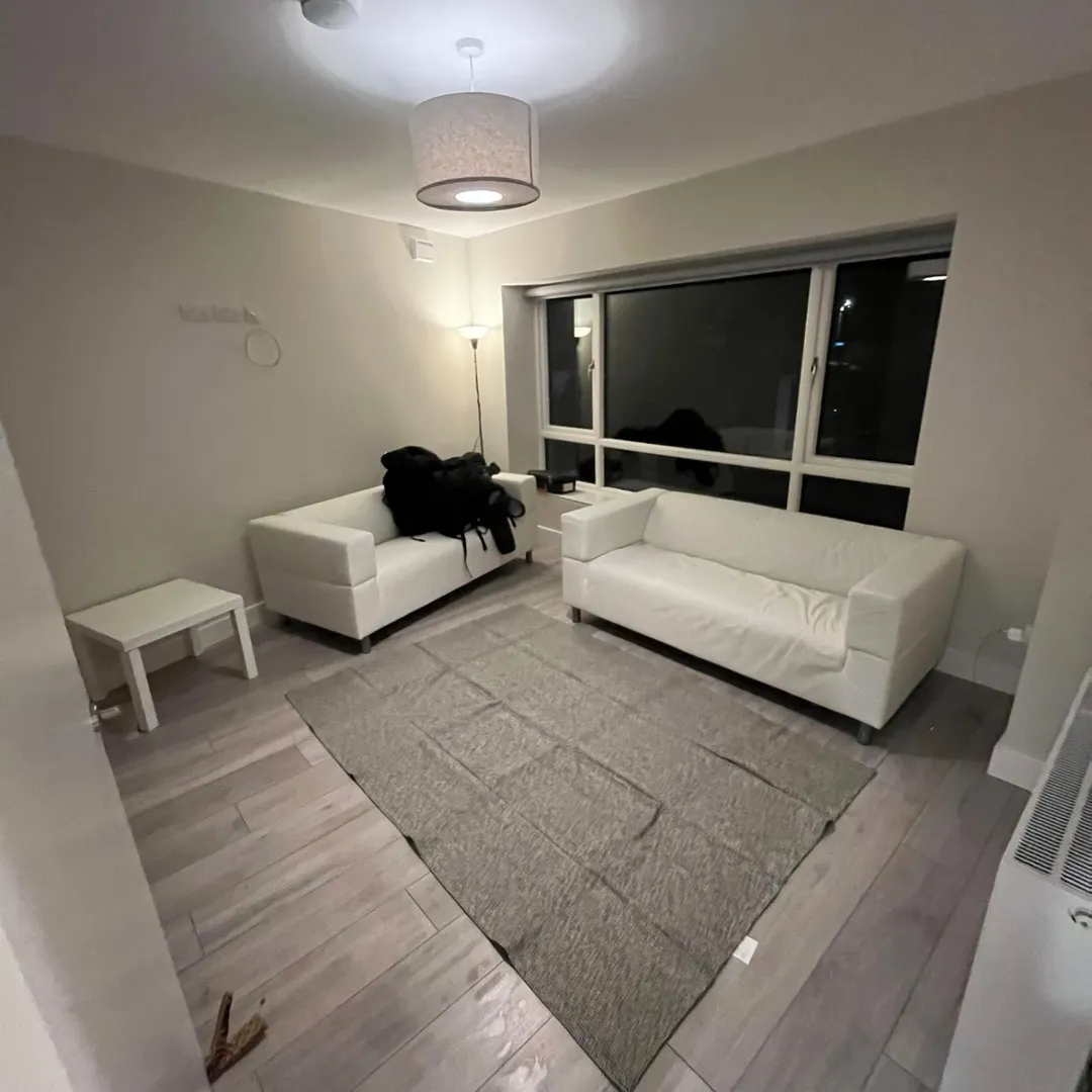 Modern living room with white sofas, gray rug, and large window at night.
