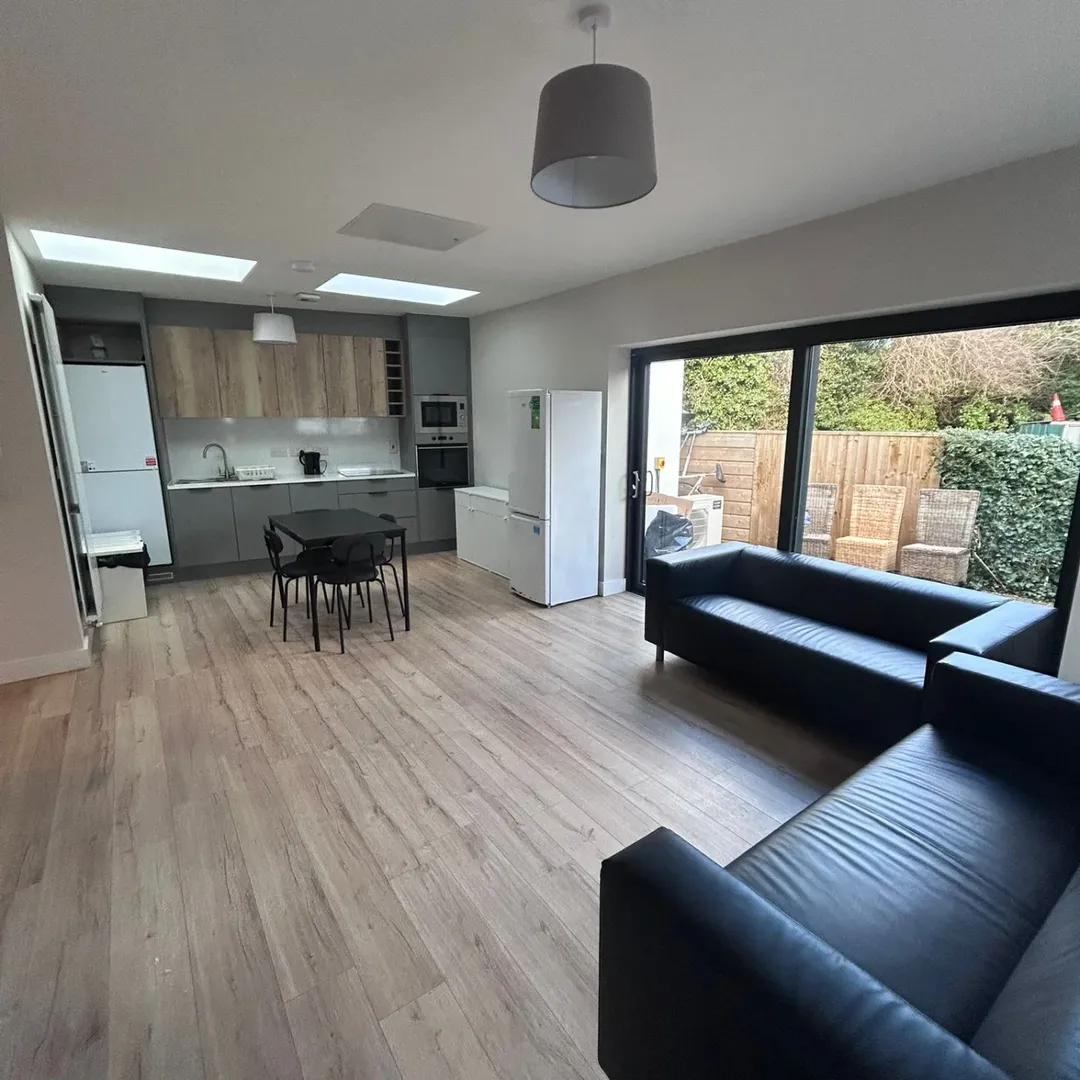Modern Open Plan Kitchen Living Area Open-plan kitchen and living area with black seating, table, and modern appliances. Large sliding doors to garden.