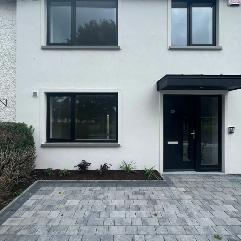 Modern white house exterior with black windows, door, and gray brick driveway.