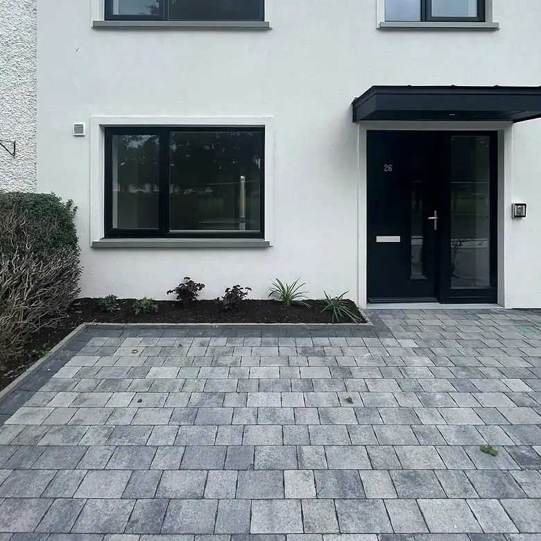 Modern white house with black framed windows and gray brick driveway.