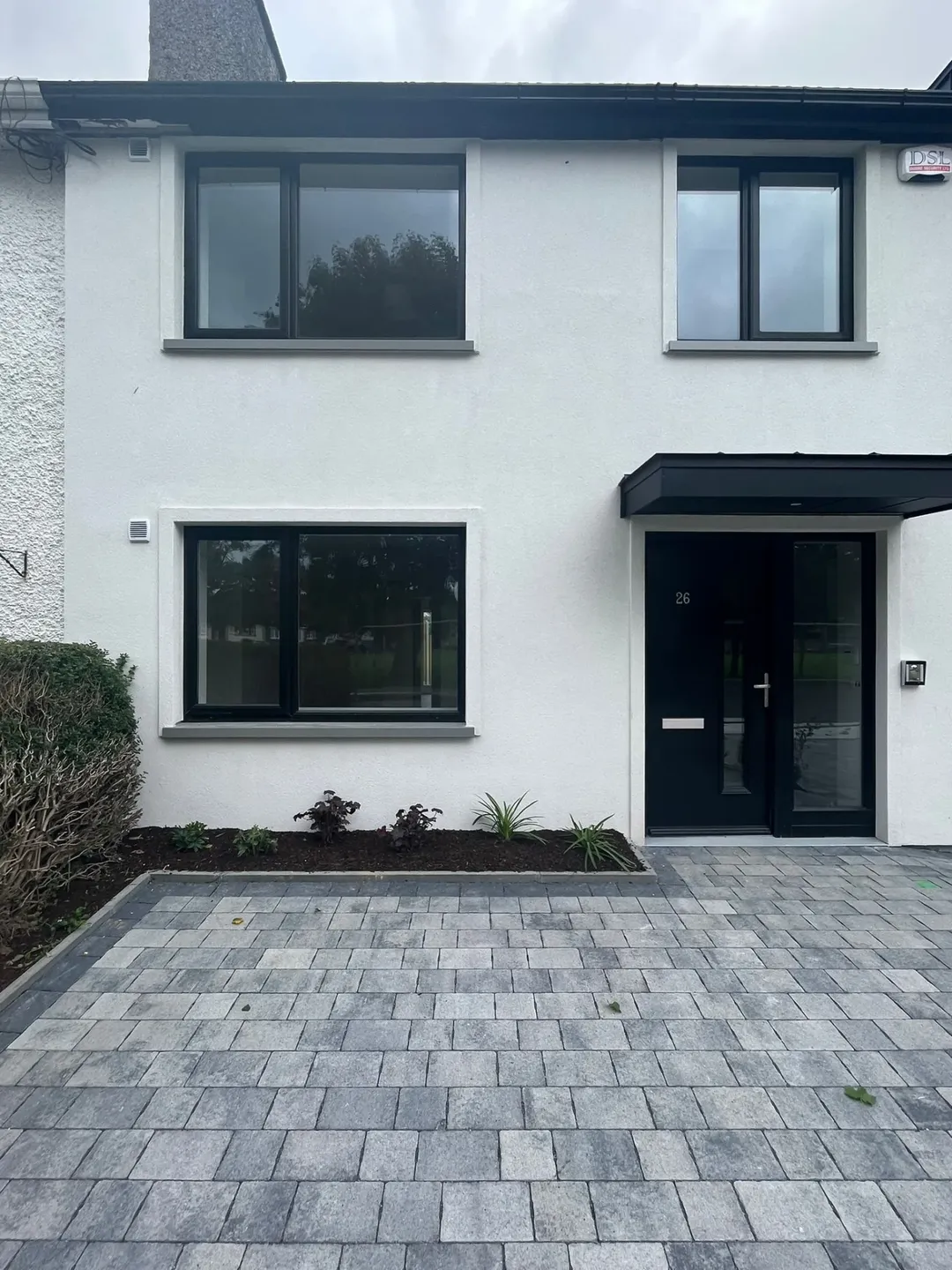 Modern white house with black framed windows and gray brick driveway.