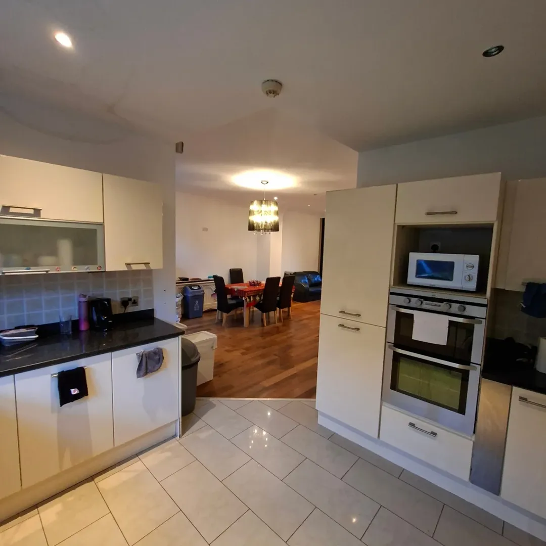 Modern kitchen with white cabinets, black countertops, and dining area in background.