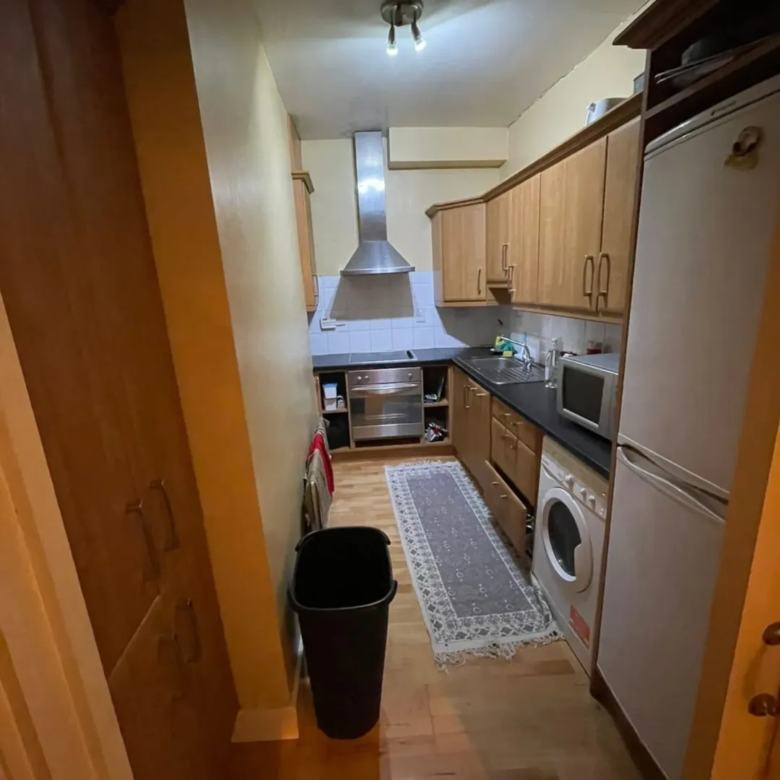 Narrow galley kitchen with wood cabinets, stainless steel hood, and white appliances.