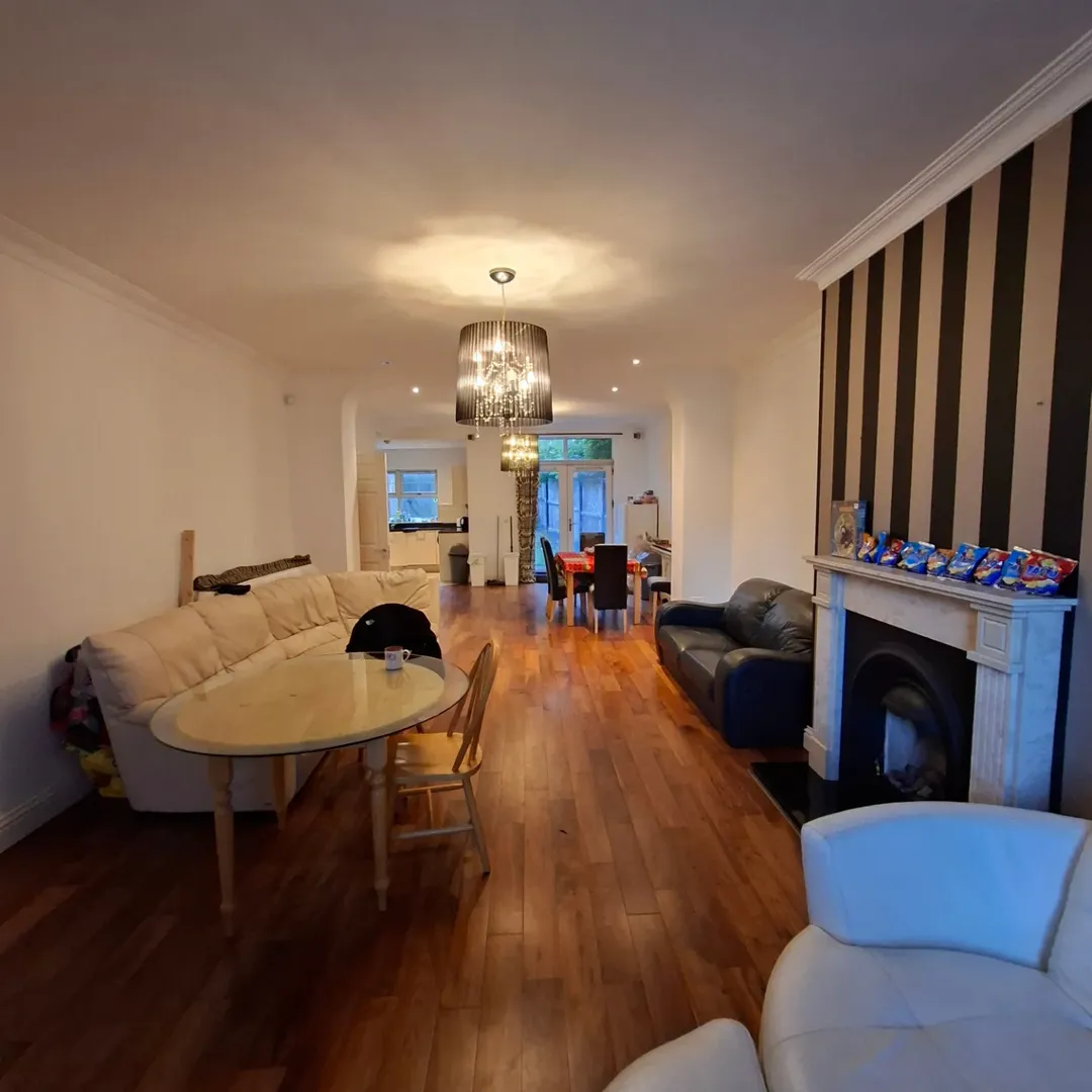 Open-plan living room with sofas, dining table, and fireplace. Modern chandelier and hardwood floors.