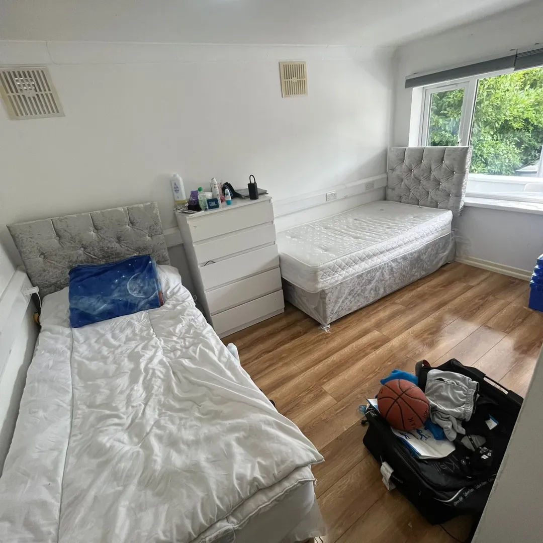 Shared bedroom with two beds, dresser, wood floor, and window with natural light.
