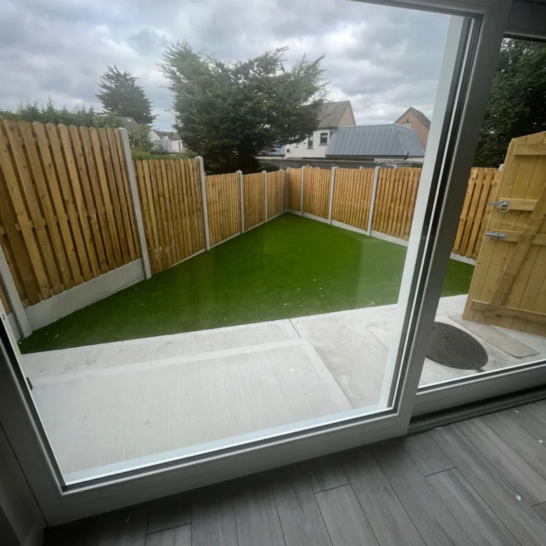 Small backyard with artificial grass, wooden fence, and concrete patio.