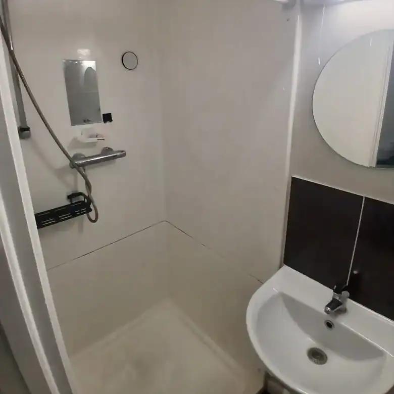 Compact bathroom featuring a shower stall and sink with mirror.