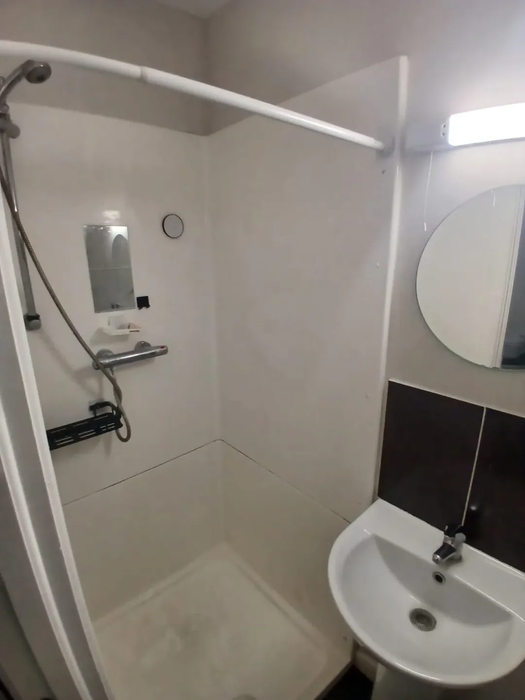 Compact bathroom featuring a shower stall and sink with mirror.